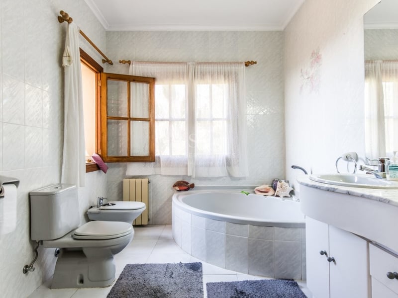 Salle de bain spacieuse avec une grande baignoire d'angle, un meuble-lavabo en marbre, des toilettes, un bidet et des fenêtres en bois.