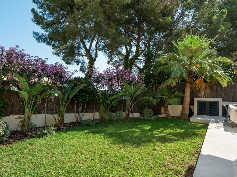 Jardin privé avec pelouse impeccable, plantes tropicales et terrasse en pierre avec table à manger ensoleillée.