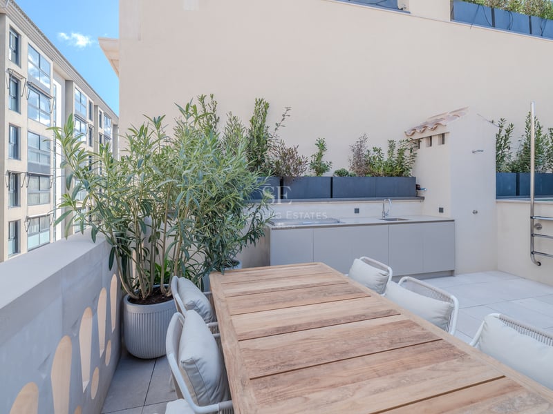 Terrasse moderne sur le toit avec table en bois, kitchenette extérieure et jardinières sous un ciel bleu.