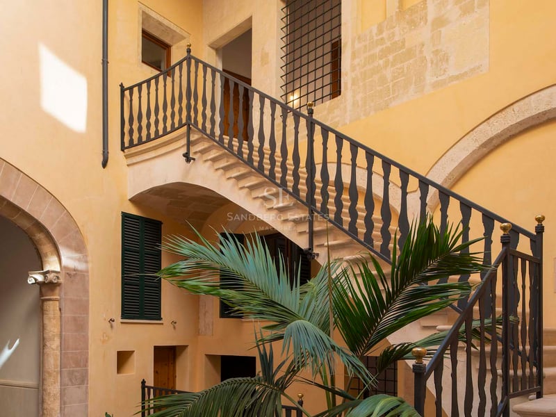 Cour traditionnelle aux murs jaunes, escalier en pierre avec rampe en fer et un palmier central.