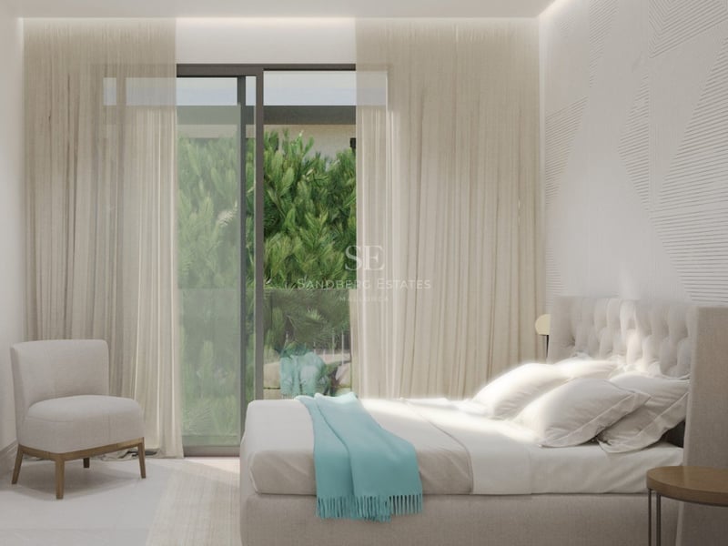 Chambre lumineuse avec tête de lit capitonnée, mur texturé et baies vitrées donnant sur la verdure.