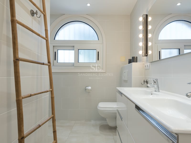 Salle de bain contemporaine avec double vasque blanche, fenêtre en arche et échelle décorative en bambou.