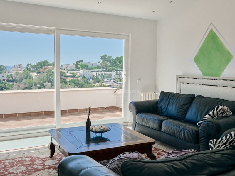 Salon moderne avec canapés en cuir noir et grandes baies vitrées s'ouvrant sur une terrasse surplombant les collines.