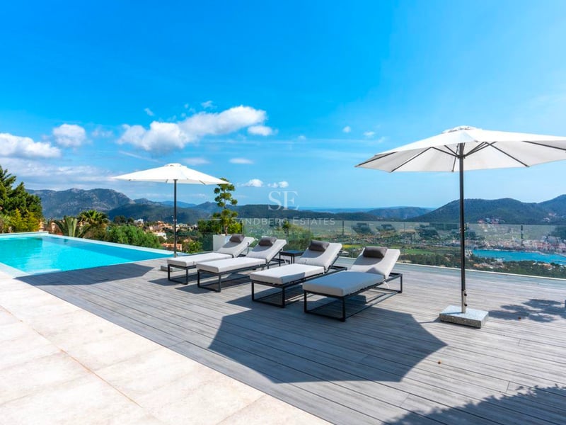 Piscine à débordement sur terrasse en bois avec bains de soleil gris, parasols blancs et vue mer et montagne.