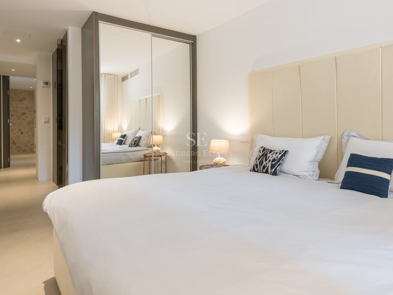 Chambre lumineuse avec un grand lit, tête de lit en tissu crème et placards à portes miroirs.
