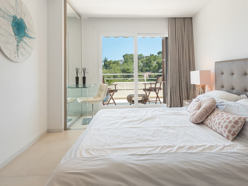 Chambre contemporaine lumineuse avec bureau en verre, tête de lit en cuir et accès direct à un balcon privé.