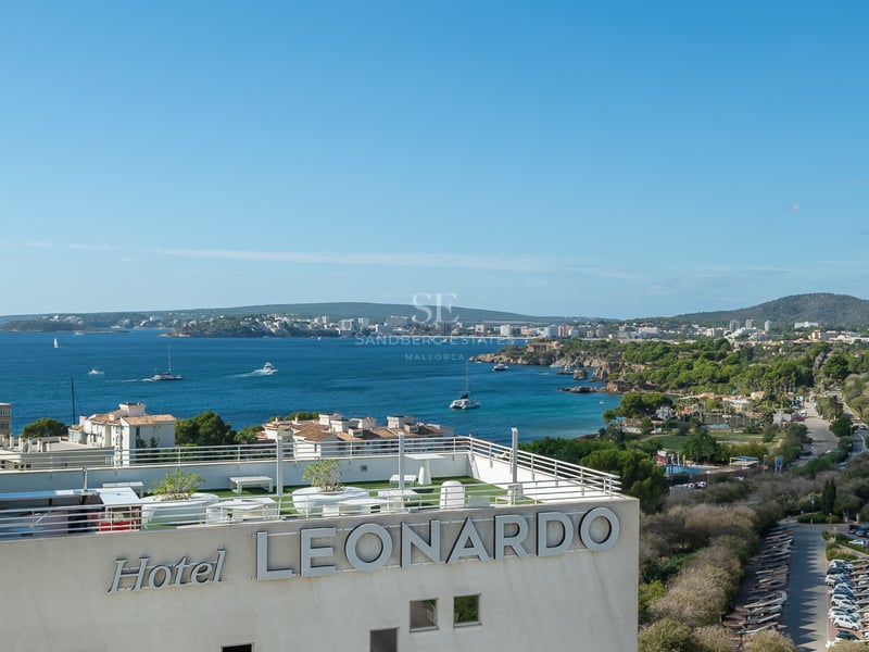 Vue panoramique d'une baie méditerranéenne et du littoral depuis un toit-terrasse moderne avec garde-corps blancs.