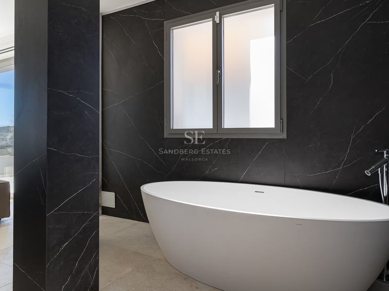 Salle de bains moderne avec baignoire ovale blanche contre un mur en marbre noir veiné et une fenêtre dépolie.