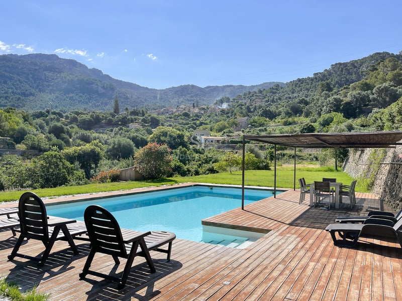 Piscine rectangulaire entourée d'une terrasse en bois avec transats et coin repas ombragé sous une pergola.