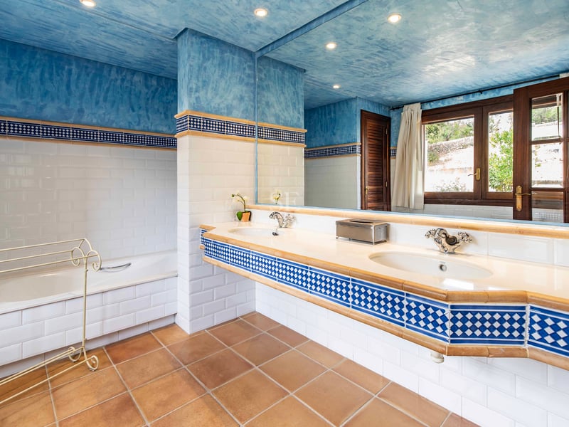Salle de bain avec plafond bleu texturé, sol en terre cuite, double vasque et baignoire encastrée.