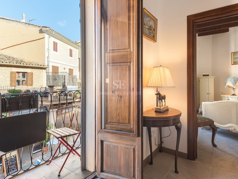 Chambre classique avec lit orné vue depuis un couloir à côté d'un balcon donnant sur une rue méditerranéenne.