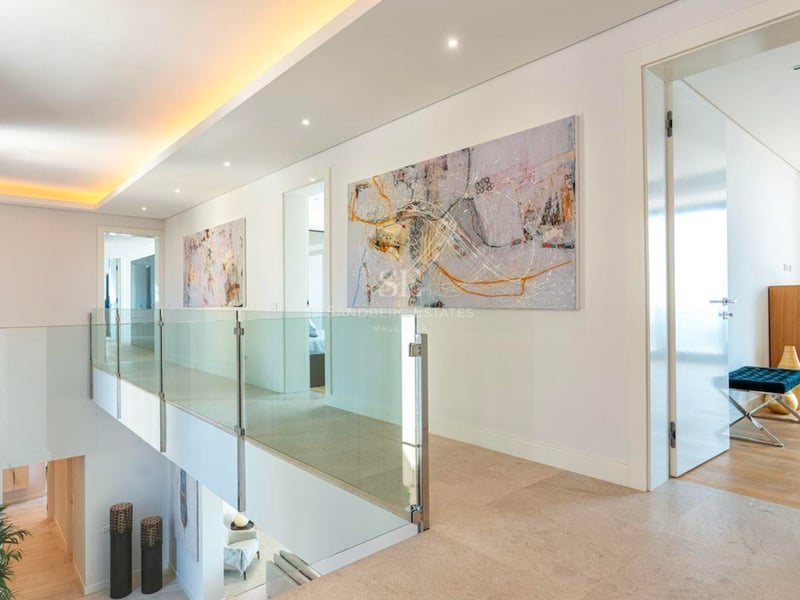 Couloir moderne avec balustrades en verre, art abstrait et sols en pierre surplombant l'étage inférieur.