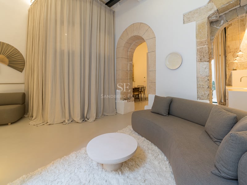 Salon contemporain doté d'un canapé incurvé gris, d'un tapis blanc à poils longs et de grandes arches en pierre rustiques.
