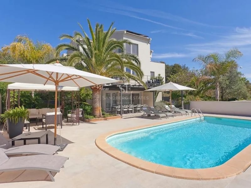 Piscine de luxe aux eaux turquoise, terrasse en pierre beige, chaises longues et palmiers sous un ciel bleu.