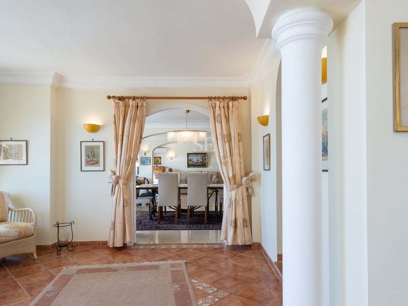 Intérieur avec sols en terre cuite, arche avec rideaux, colonne blanche et vue sur la salle à manger d'une villa.