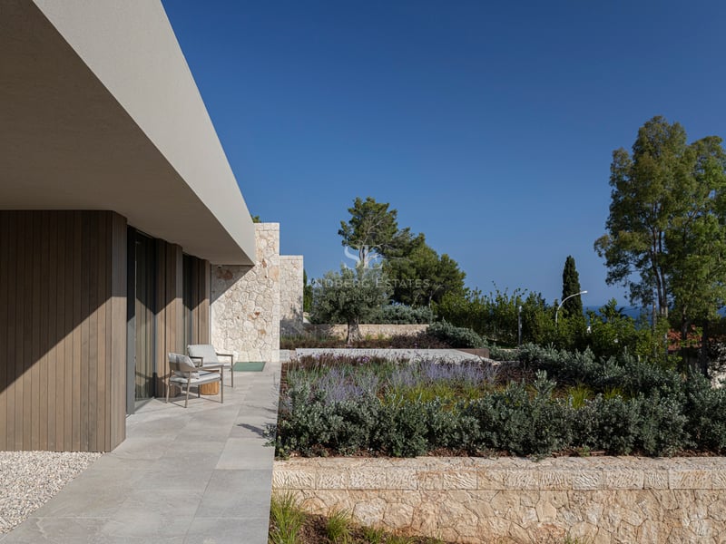 Terrasse de villa moderne avec fauteuils gris, murs en pierre naturelle et bardage en bois sous un auvent.