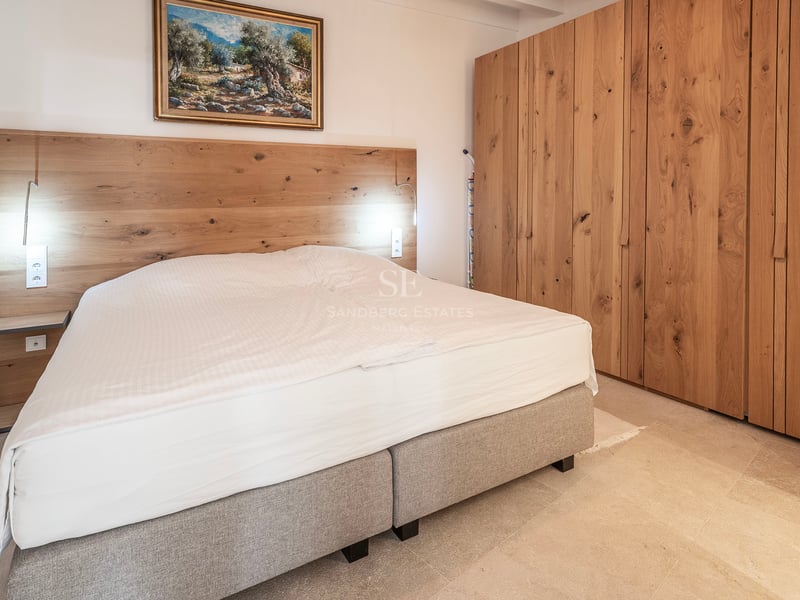 Chambre moderne avec un grand lit, une tête de lit en bois, de grandes armoires en chêne et un tableau au mur.
