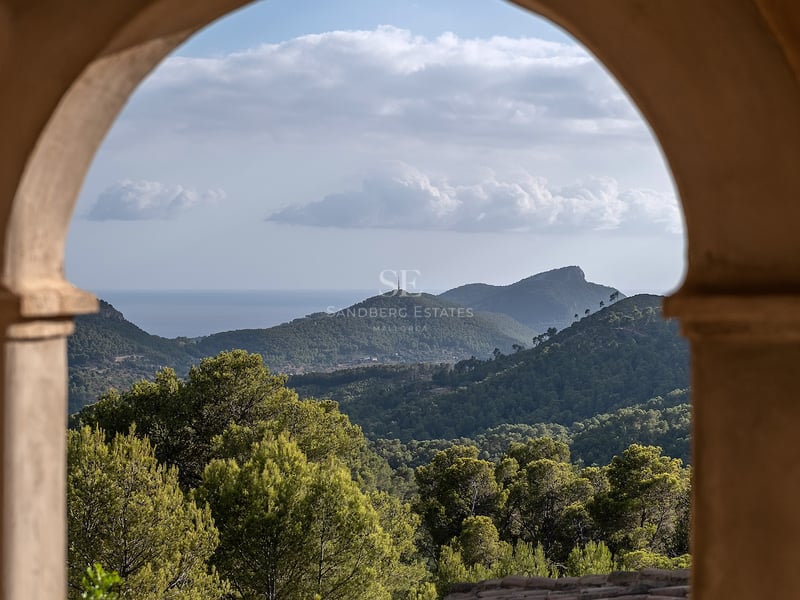 Vue de montagnes verdoyantes et de la mer au loin encadrée par une arche en pierre traditionnelle.