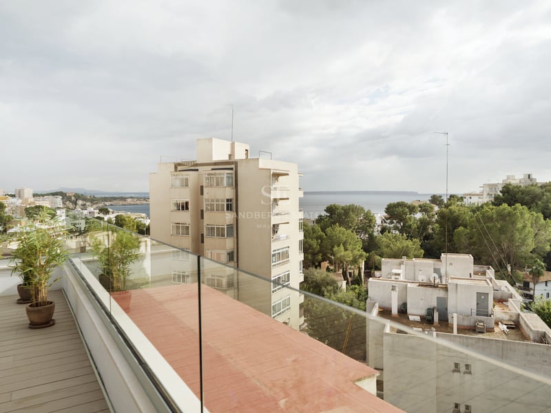 Terrasse contemporaine avec plancher en bois et garde-corps en verre surplombant une ville côtière et la Méditerranée.