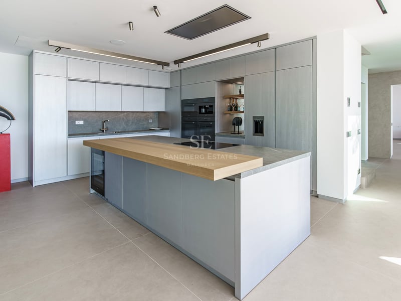 Cuisine moderne avec îlot gris, bar en bois, appareils intégrés et plans de travail en pierre grise.