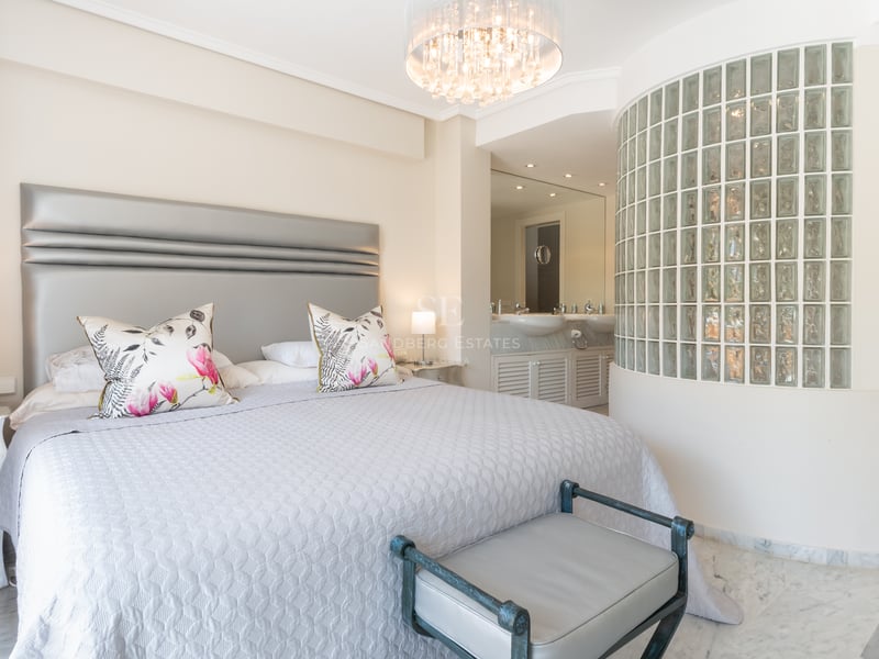 Chambre de luxe avec grand lit, sol en marbre, lustre en cristal et mur incurvé en briques de verre vers la salle de bain.