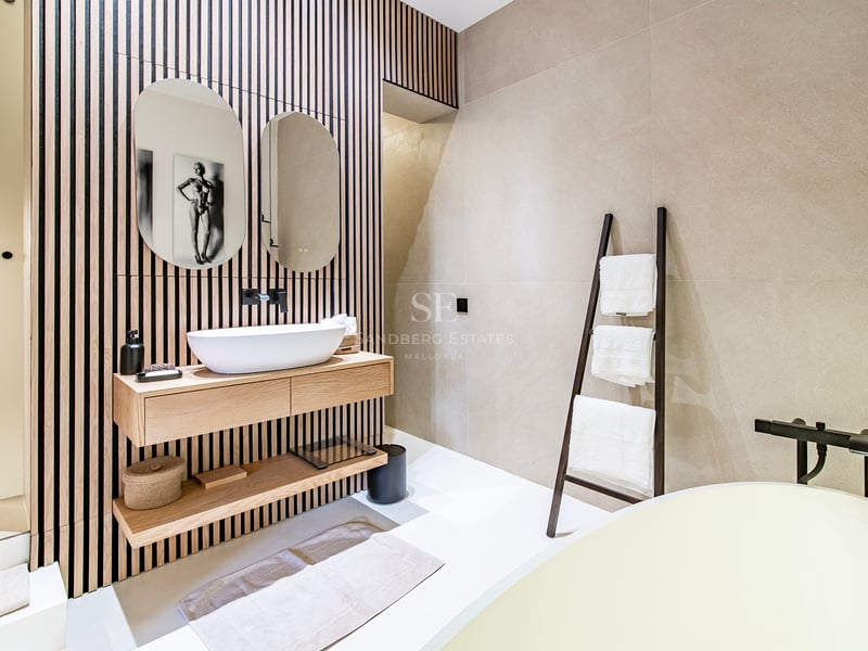 Salle de bains minimaliste avec mur en tasseaux de bois, deux miroirs ovales et meuble vasque suspendu en chêne.