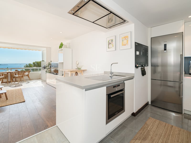 Cuisine blanche moderne avec appareils en inox, salon et terrasse donnant sur la mer Méditerranée.