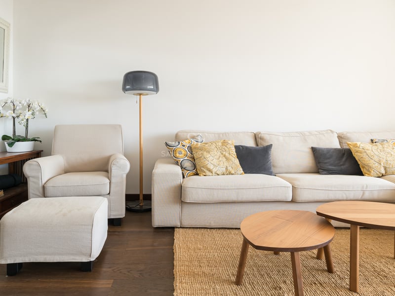 Salon lumineux avec canapé crème, tables basses en bois et tapis en jute sur parquet foncé.