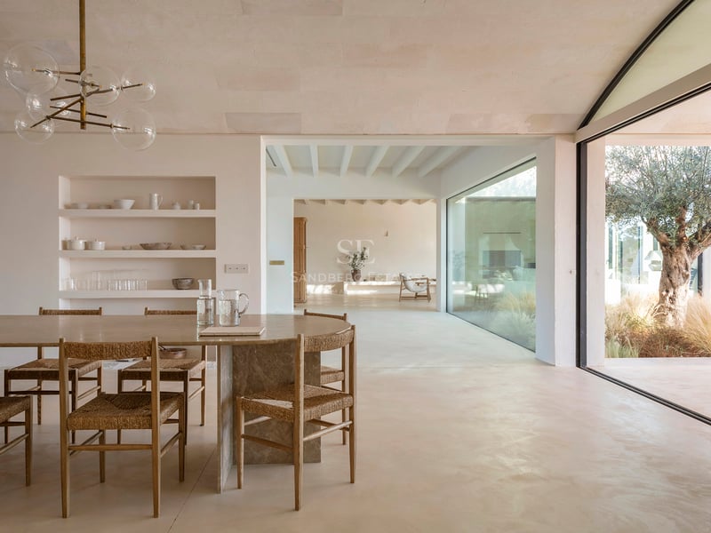 Modern dining area featuring a stone table, woven chairs, and large glass doors opening to a Mediterranean courtyard.
