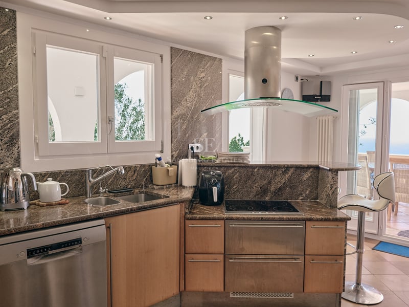 Cuisine contemporaine avec plans de travail en granit, appareils en inox et vue sur une terrasse ensoleillée.