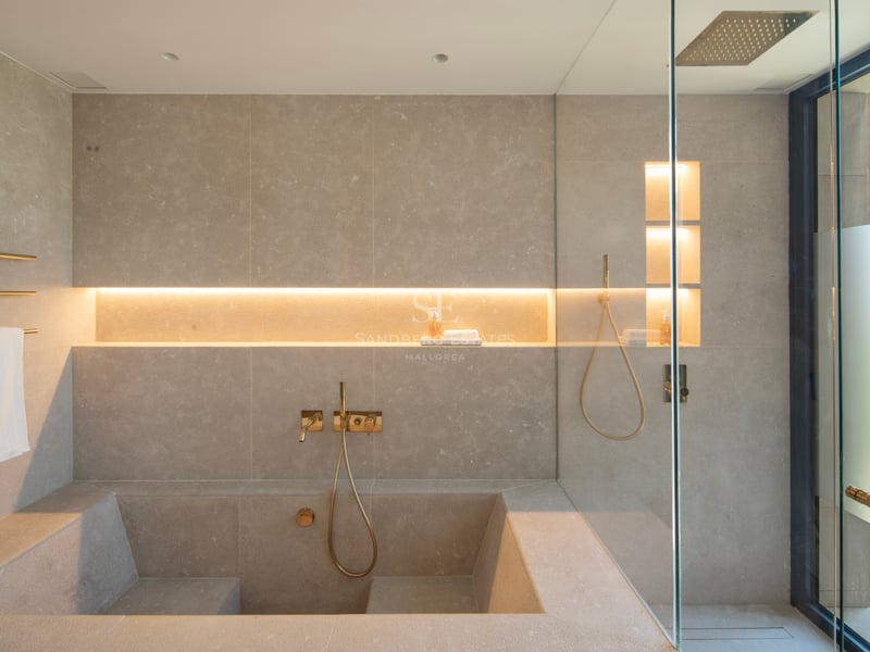 Salle de bains de luxe minimaliste avec baignoire en pierre sur mesure, douche à l'italienne et robinetterie dorée.