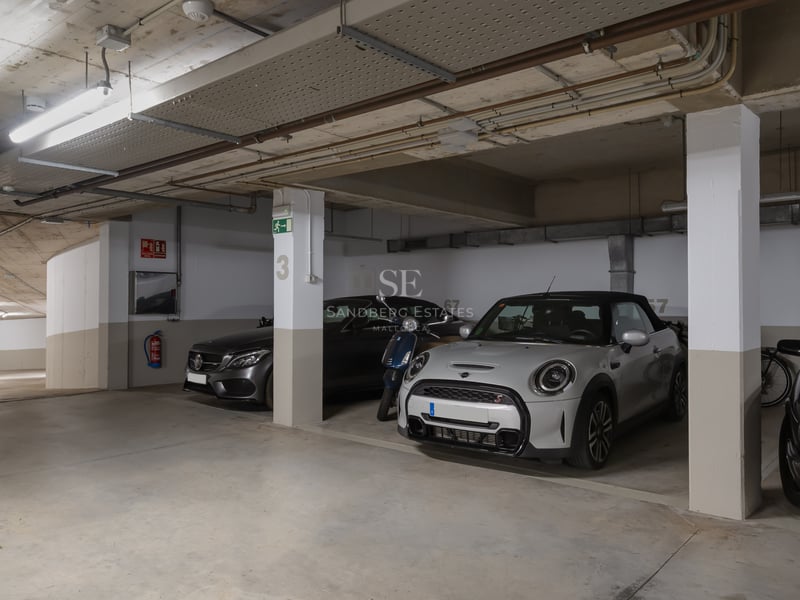 Garage souterrain lumineux avec places numérotées, piliers en béton et voitures de luxe stationnées.
