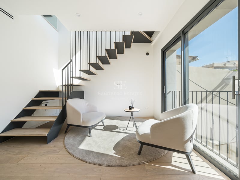 Heller Wohnraum mit zwei cremefarbenen Sesseln, rundem Teppich und einer modernen Holz-Metall-Treppe.