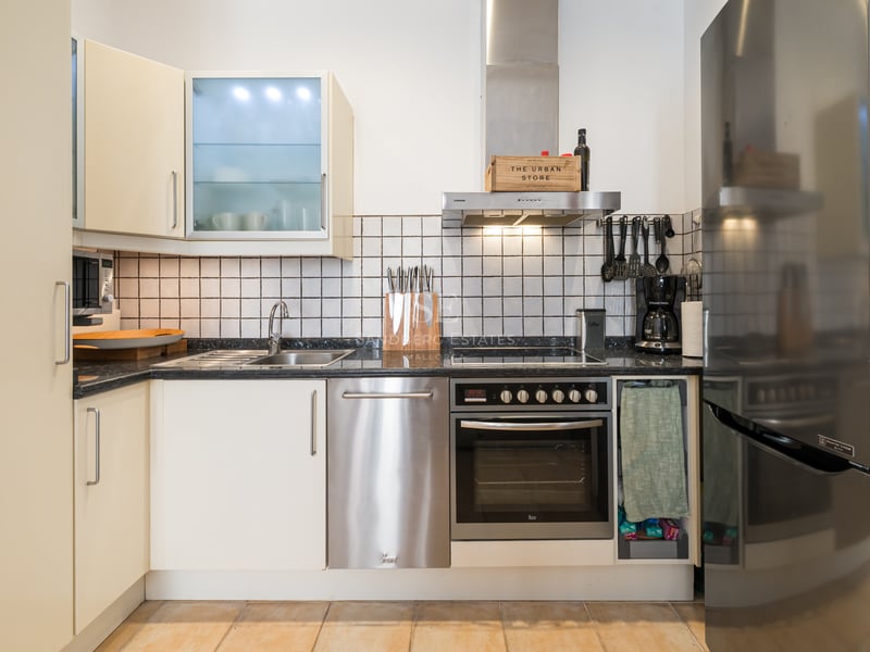 Cuisine moderne avec placards crème, électroménager en inox, plan de travail en granit noir et crédence en carrelage blanc.