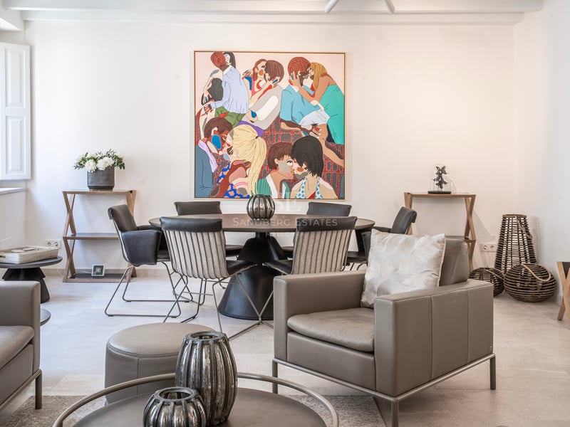 Pièce moderne lumineuse avec un fauteuil en cuir gris, une table à manger ronde et un grand tableau coloré au mur.