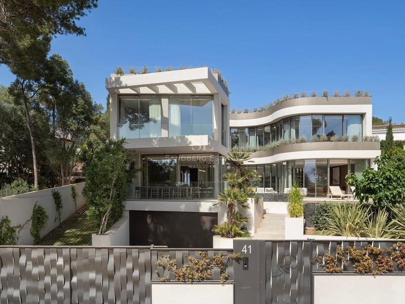 Villa contemporaine blanche de trois étages avec parois de verre courbes et entrée sécurisée sous un ciel bleu.