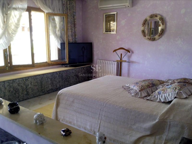 Chambre aux murs lavande avec fenêtres en bois, un lit double et des rangements intégrés sous la fenêtre.