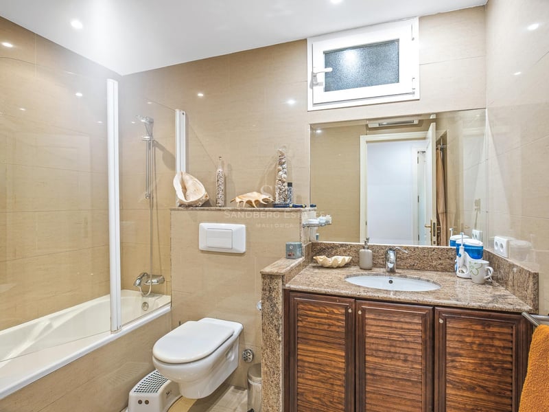 Salle de bain avec baignoire, paroi en verre, meuble en bois sombre, plan en granit et carrelage ton sable.