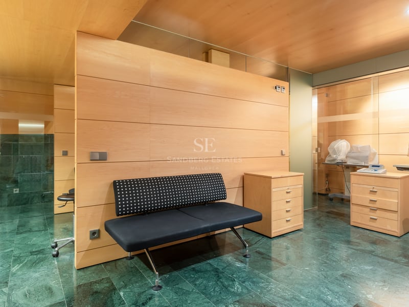 Interior with green marble flooring, light wood wall panels, a black bench, and professional consultation equipment.