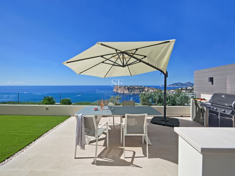 Terrasse extérieure avec table à manger, parasol, barbecue et vue imprenable sur l'océan sous un ciel bleu clair.