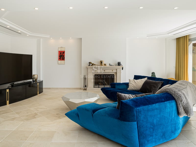Espace de vie moderne avec un grand canapé en velours bleu, cheminée en pierre et sol en pierre naturelle.