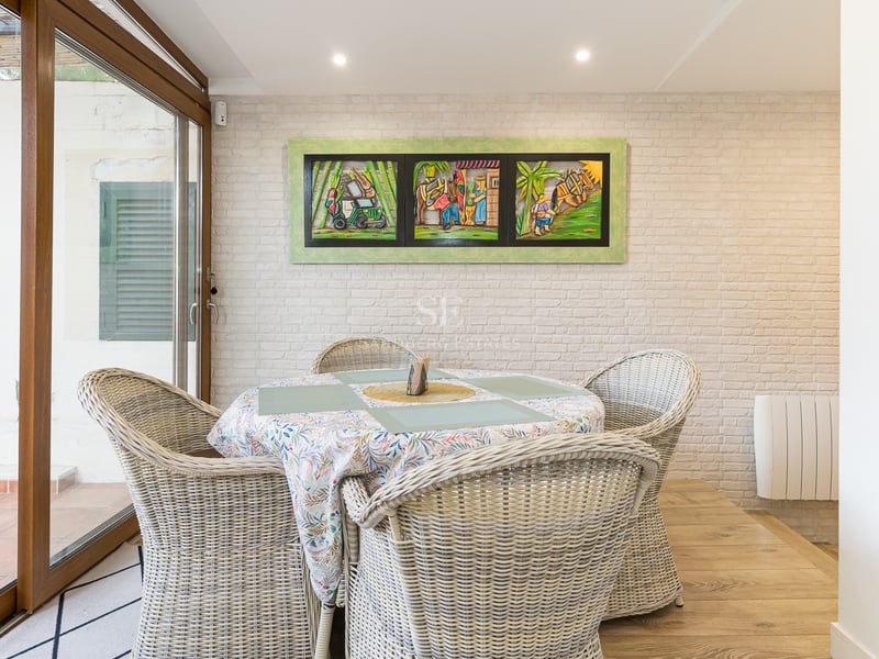 Coin repas avec chaises en osier, mur en briques blanches et baies vitrées coulissantes.