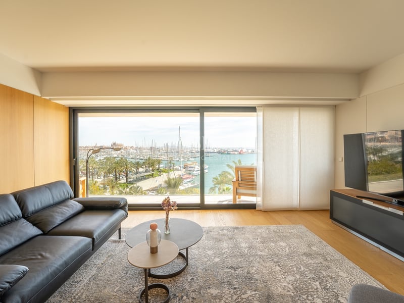 Salon contemporain avec canapé en cuir noir et grande baie vitrée offrant une vue sur un port de plaisance.