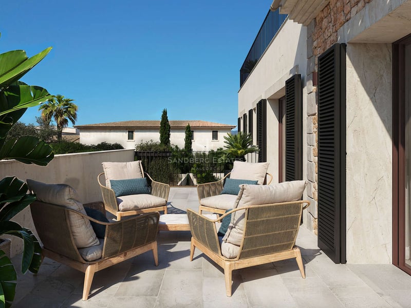 Terrasse de luxe avec quatre fauteuils tressés, coussins crème et murs en pierre naturelle avec volets.
