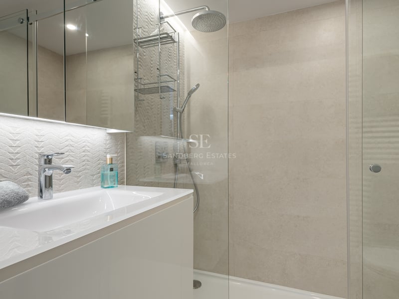 Salle de bain contemporaine avec douche vitrée, vanité blanche et carrelage mural texturé crème.
