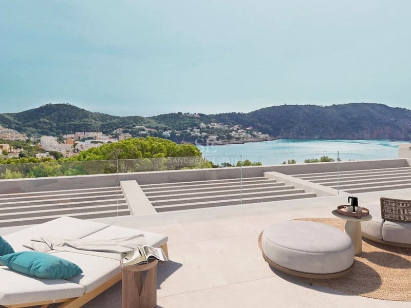 Terrasse moderne en pierre avec chaises longues et mobilier design surplombant une baie méditerranéenne et des montagnes.