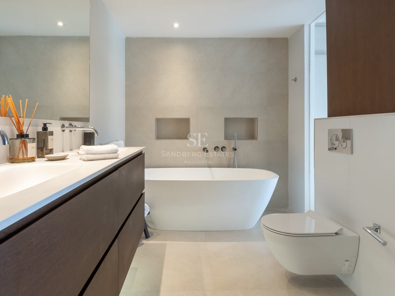 Salle de bains minimaliste avec baignoire îlot blanche, meuble en bois foncé et carrelage beige.