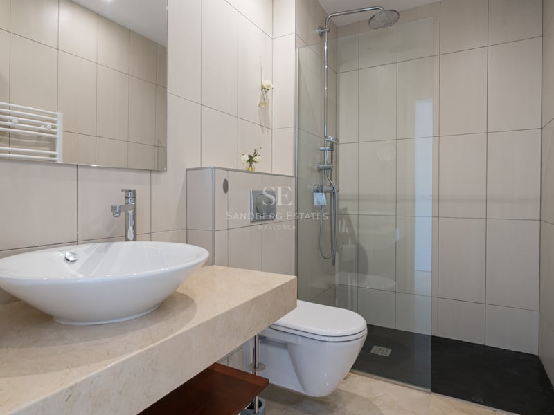 Salle de bain moderne avec carrelage beige, plan en marbre, vasque à poser et douche avec paroi vitrée.