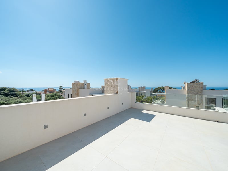 Grande terrasse de toit carrelée de blanc avec balustrade en verre, surplombant des villas modernes et l'océan.