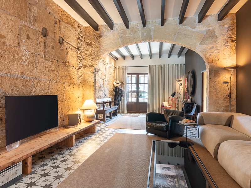 Modern living room featuring original stone walls, arched ceiling, exposed beams, and patterned hydraulic tiles.